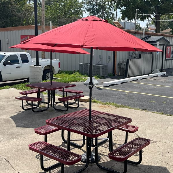Outdoor seating area at Home Slice Pizzeria with red picnic tables and matching umbrellas.