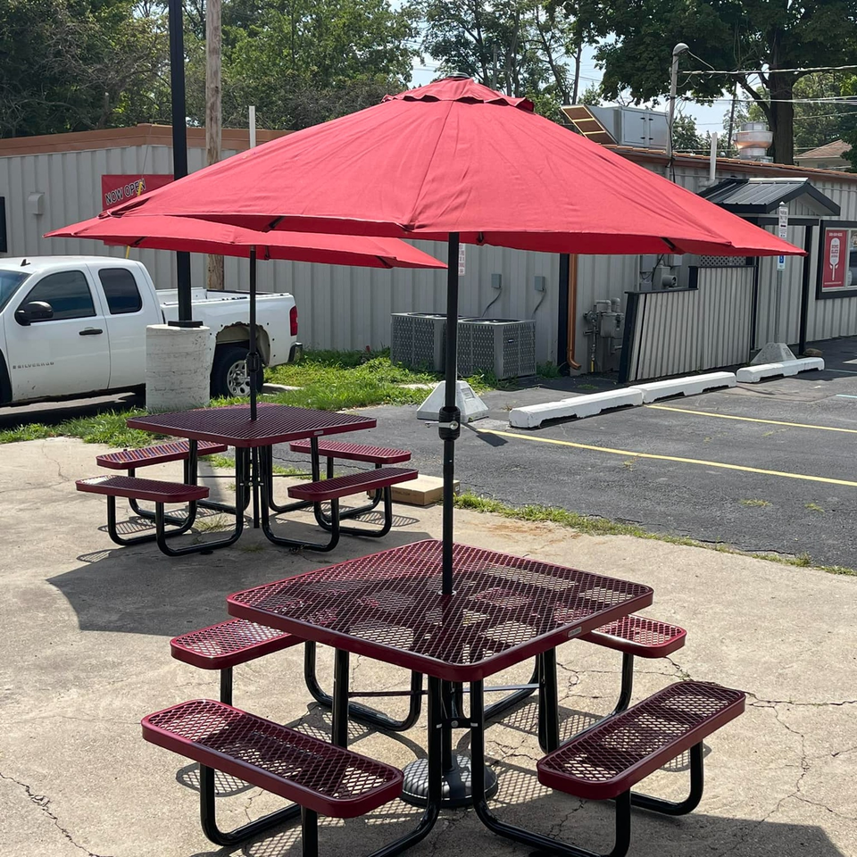 Outdoor seating area at Home Slice Pizzeria with red picnic tables and matching umbrellas.