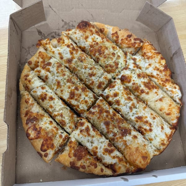 Cheesy garlic breadsticks, cut into strips, in a Home Slice Pizzeria cardboard box.