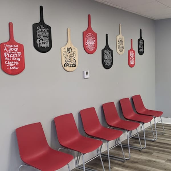 A waiting area with red chairs and pizza-themed decorative paddles on a gray wall.