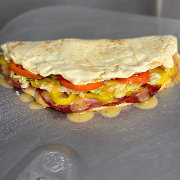A Home Slice Pizzeria calzone, filled with melted cheese, pepperoni, tomatoes, lettuce, and banana peppers.
