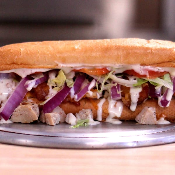 A Home Slice Pizzeria sub sandwich filled with chicken, red onions, lettuce, tomatoes, and white sauce.