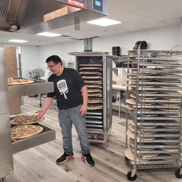 A Home Slice Pizzeria employee places an uncooked pizza into a large commercial oven.