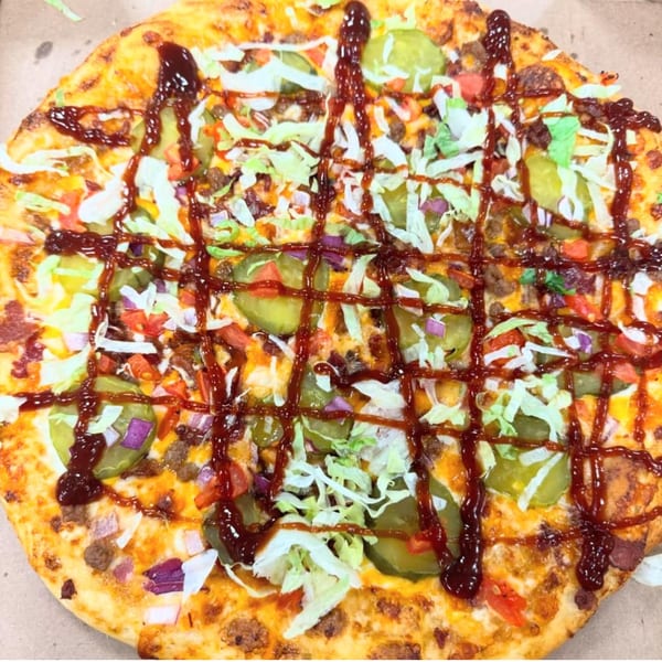 A Home Slice Pizzeria pizza topped with ground meat, pickles, lettuce, and barbecue sauce.